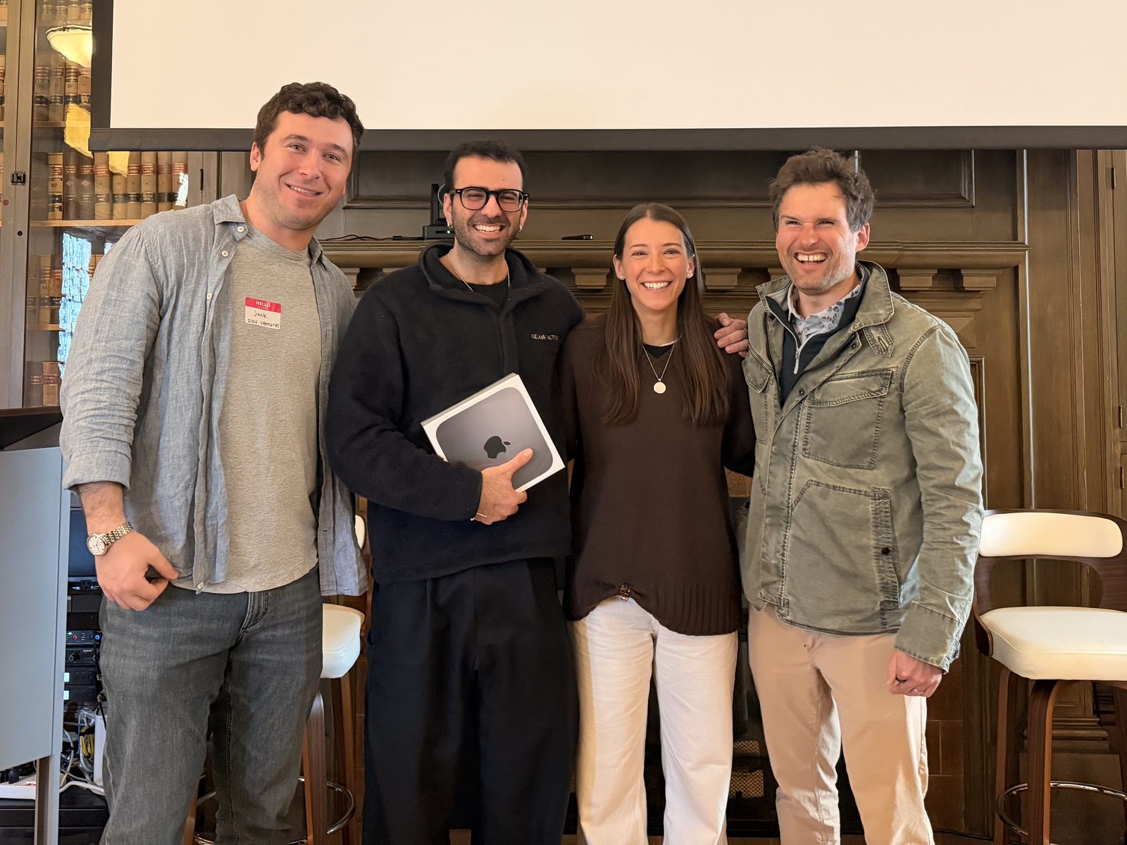 Four hackathon participants smiling together, one holding a Mac mini prize